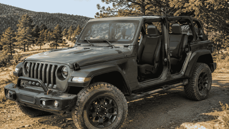 A Jeep Wrangler with the doors off parked on a dirt trail, showing the interior with clean dark seat covers installed