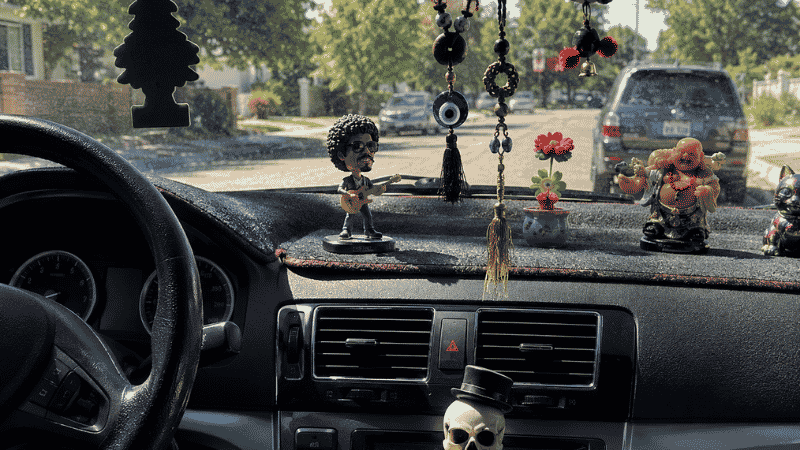 A cluttered car dashboard with too many decorative accessories including hanging ornaments, dashboard toys, and unnecessary gadgets