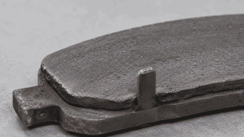 Worn brake pad with the metal wear indicator tab visible, the component that causes the squealing warning sound