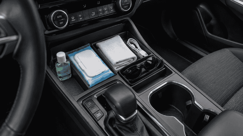 Car center console organizer holding hand sanitizer, sanitizing wipes, charging cable, sunglasses, and microfiber cloth