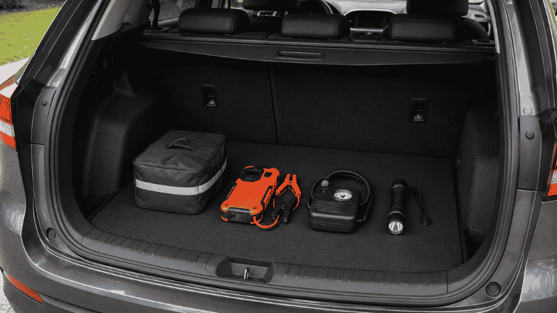 A neatly organized car trunk with a jump starter, emergency kit bag, tire inflator, and flashlight arranged inside