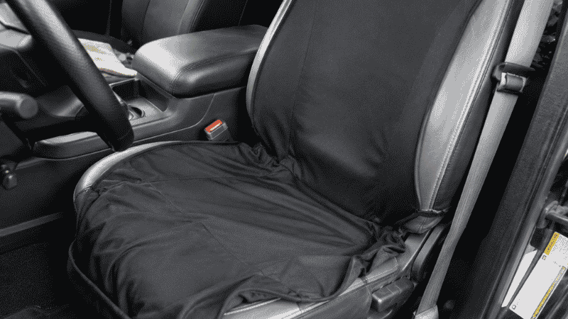 A poorly fitting universal seat cover bunching and shifting on a car seat, exposing the original seat fabric underneath