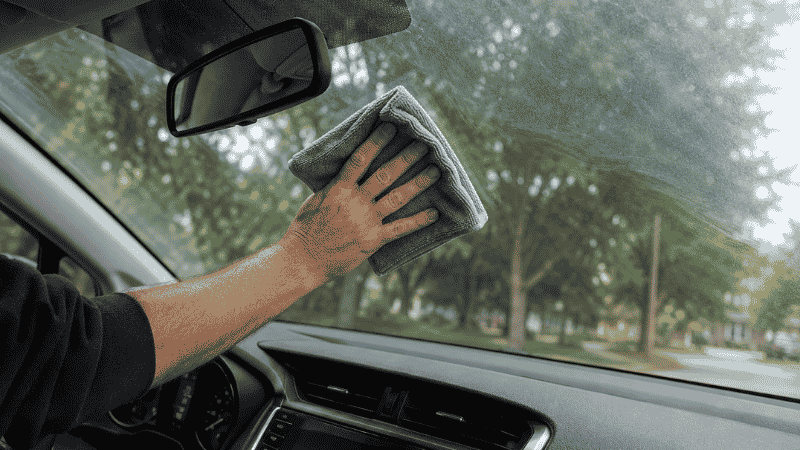 Cleaning the inside of a car windshield with a microfiber cloth and ammonia-free glass cleaner
