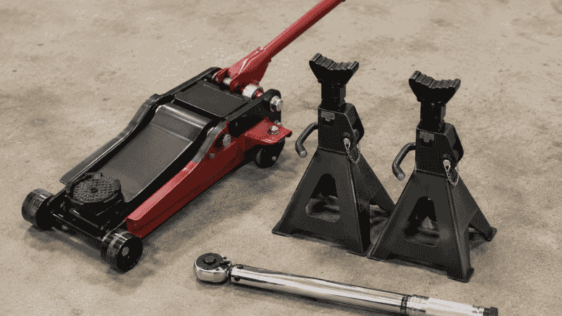 DIY tire rotation tools laid out on a garage floor: a floor jack, two jack stands, and a torque wrench