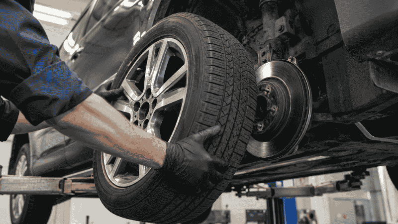 A mechanic removing a car tire from the wheel hub during a professional tire rotation service at an auto shop