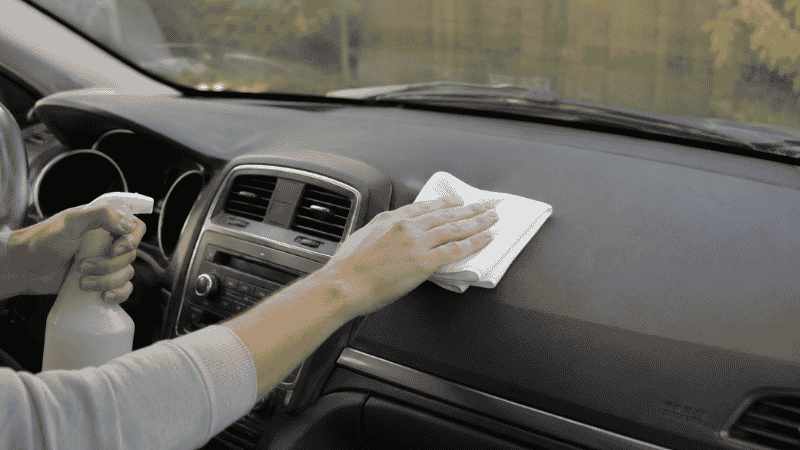 A person cleaning the inside of a car with a microfiber cloth and interior spray