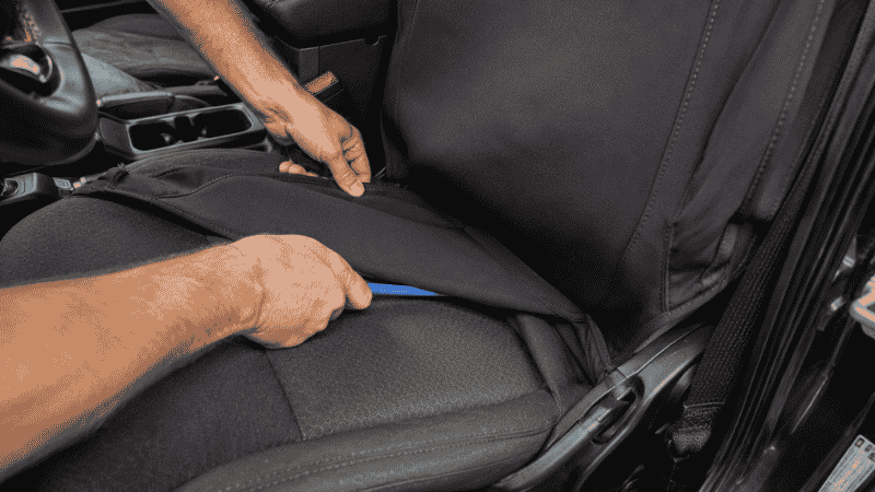 Person's hands tucking a seat cover into the gap between a Jeep car seat cushion and backrest during installation