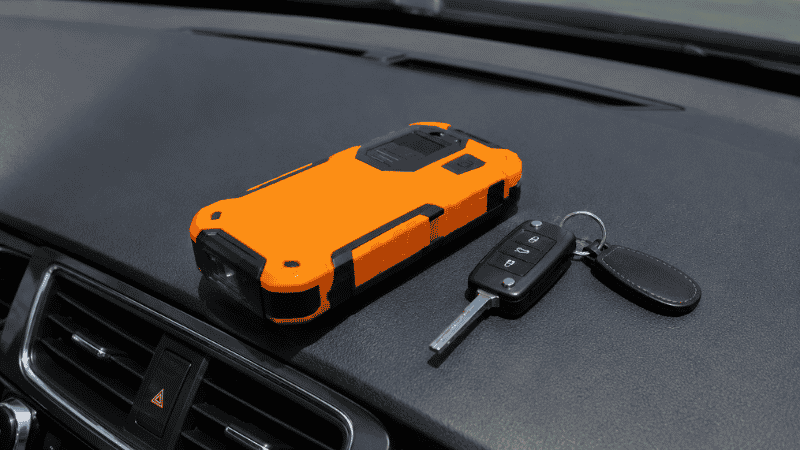 A compact portable lithium jump starter sitting on a car dashboard next to a set of car keys
