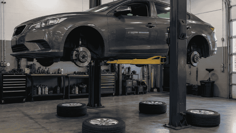 A car raised on a hydraulic lift at an auto repair shop with all four wheels removed for a professional tire rotation service