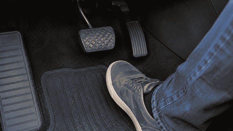 A driver's foot gently resting above the brake pedal on the floor mat, demonstrating proper brake pedal technique without resting on the pedal