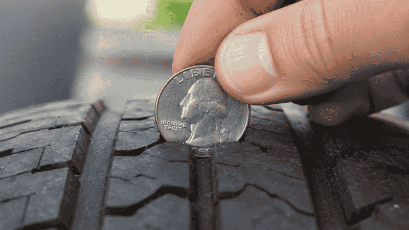 A hand inserting a quarter coin into a car tire tread groove to check tread depth using the quarter test method
