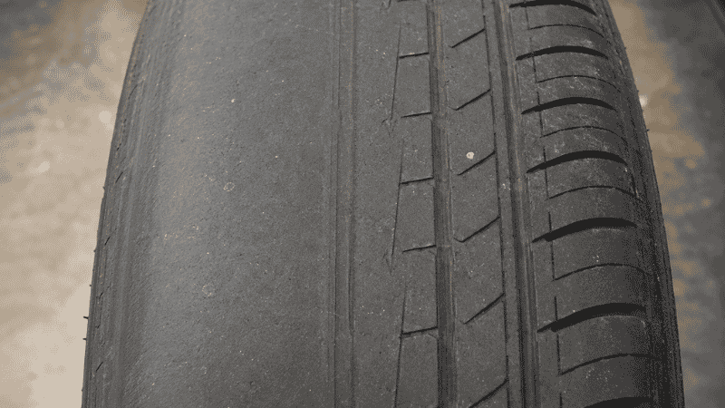 A car tire showing uneven edge wear on the inner shoulder indicating wheel alignment problems