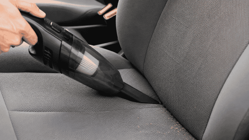 Using a handheld vacuum with a crevice tool to clean the gap between car seat cushion and backrest
