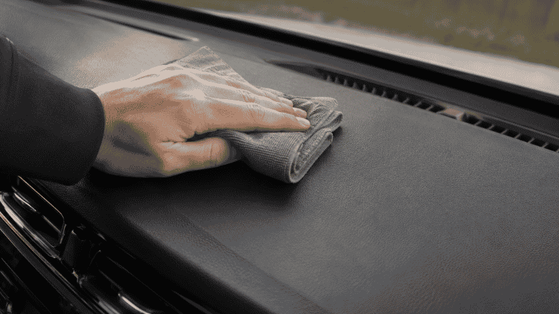 Wiping a car dashboard with a folded microfiber cloth to remove dust and grime