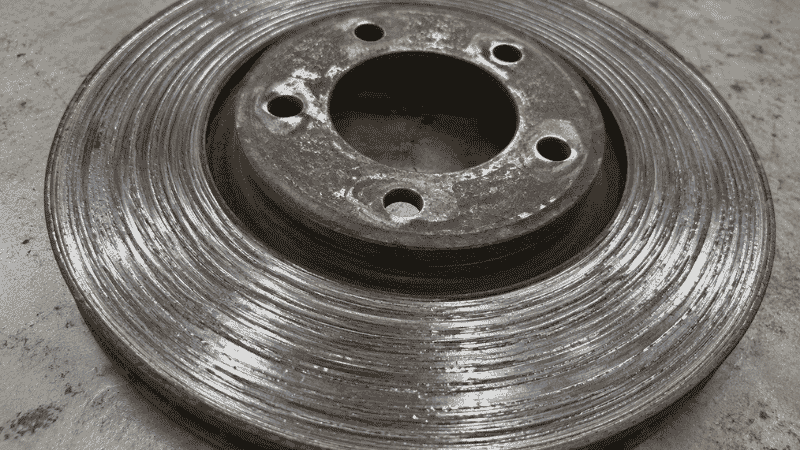 A severely worn brake rotor with visible deep grooves and scoring marks caused by metal-on-metal contact from a completely worn brake pad