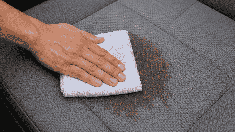 A person pressing a white microfiber cloth straight down onto a stain on a car fabric seat to blot it, demonstrating the correct blotting technique