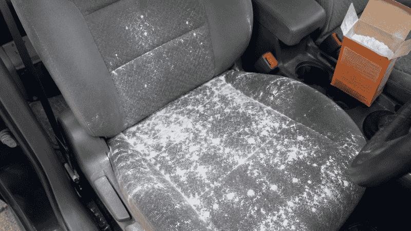 A person leaning into a car interior sniffing to identify the source of a bad smell, checking the seats and carpet area