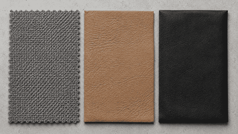 Three car seat material samples side by side: gray fabric cloth, tan genuine leather, and black faux leather leatherette