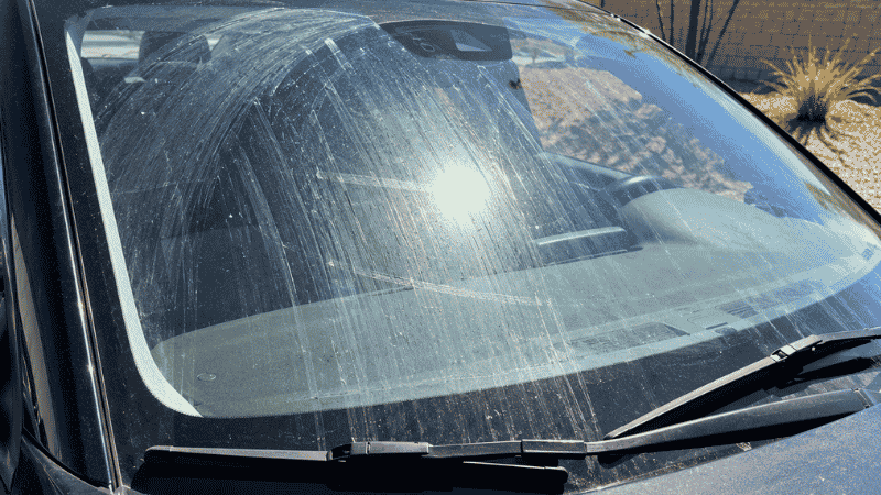A car windshield showing heavy streak marks in direct sunlight, illustrating what happens when windows are cleaned in hot sunny conditions