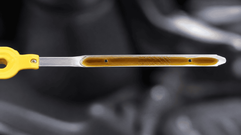 A close-up of an engine oil dipstick showing the oil level between the MIN and MAX marks with light brown healthy oil color