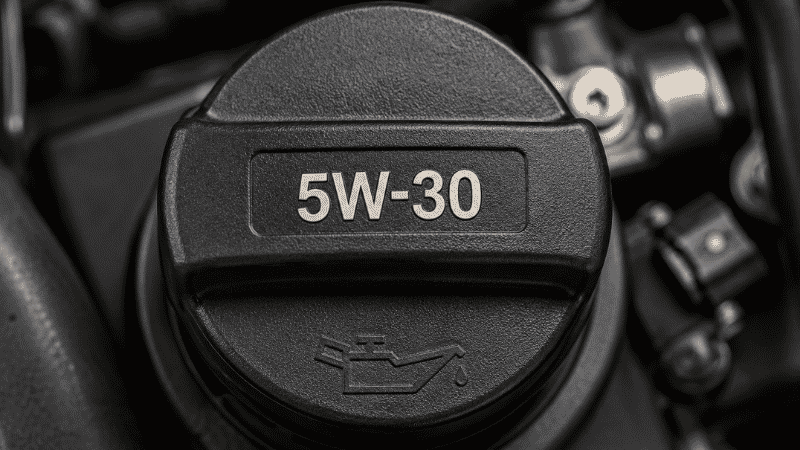 A car engine oil filler cap showing the recommended oil viscosity code 5W-30 embossed on the cap surface