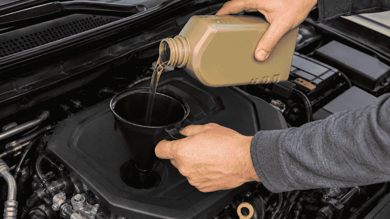 A person pouring new motor oil into a car engine through the oil filler cap using a funnel during a DIY oil change