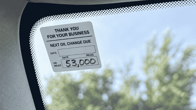 A car windshield oil change reminder sticker showing a 3,000 mile interval recommendation, illustrating the outdated advice that costs drivers money