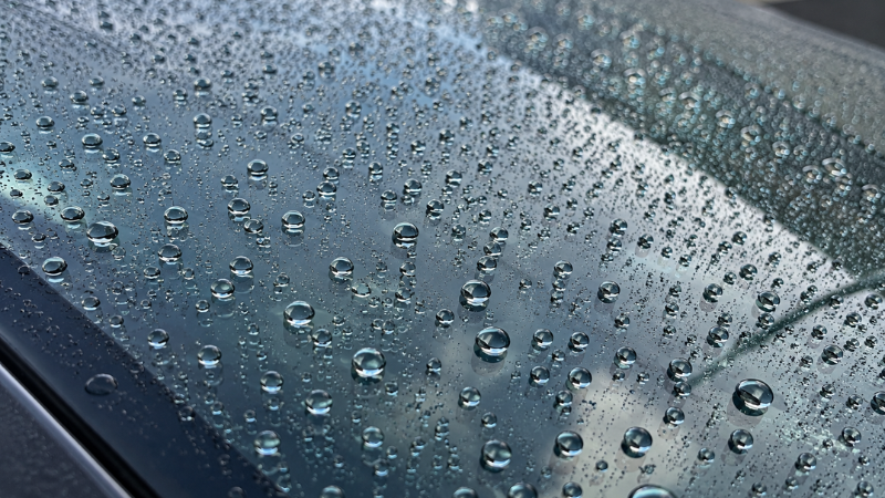 Water droplets beading perfectly on a car windshield that has been treated with a hydrophobic glass coating, showing the water-repellent effect