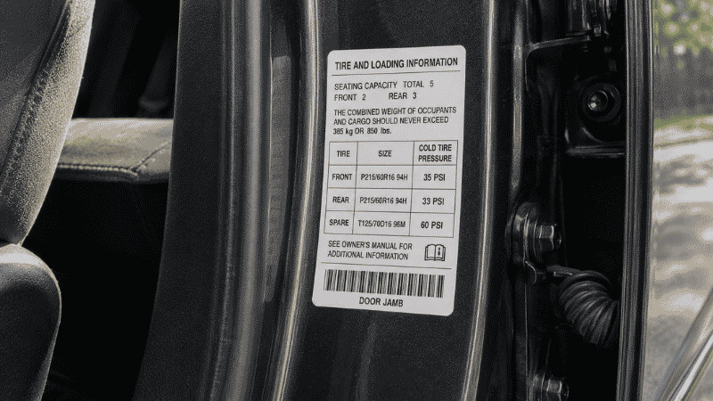 A close-up of the tire pressure information sticker on the inside of a car driver's door jamb showing recommended front and rear tire pressure in PSI
