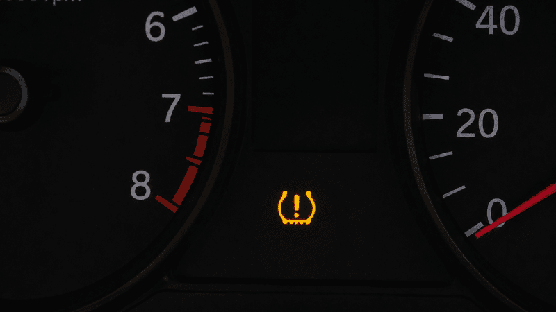 A car dashboard showing the orange TPMS tire pressure warning light illuminated, indicating low tire pressure in at least one tire