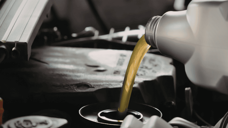 A person using a specialized threaded funnel to pour engine oil into the filler neck without spilling on the hot engine.