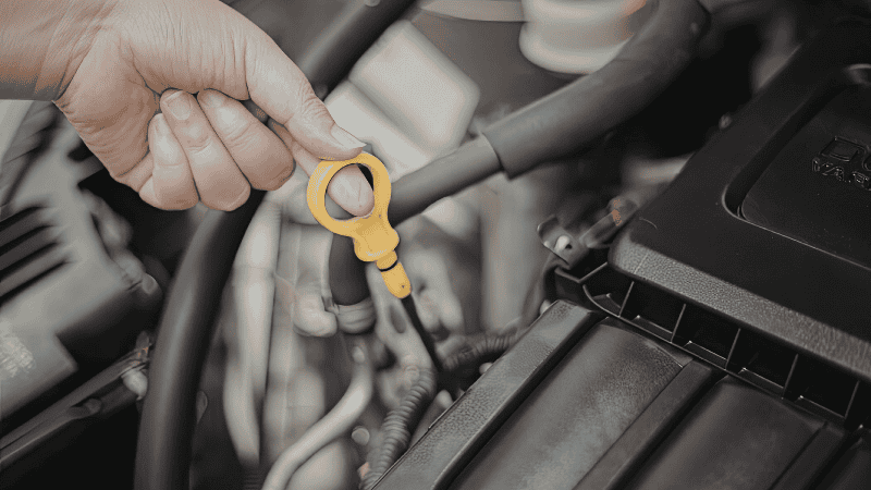 A driver pulling a yellow-handled dipstick to check the engine oil level in a clean car engine bay.