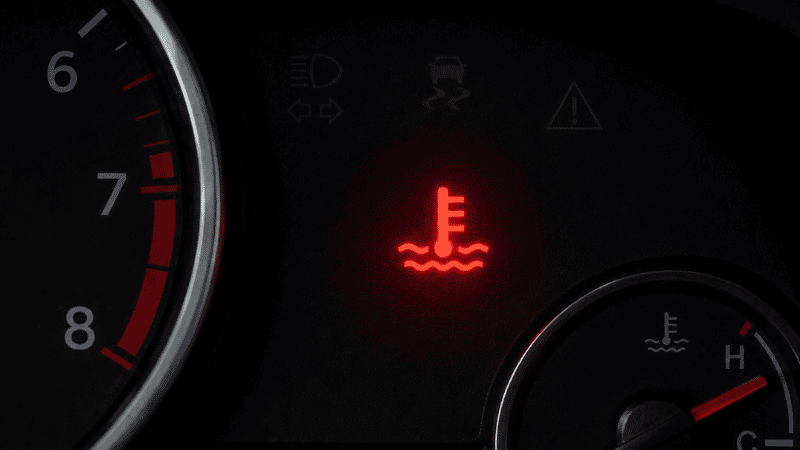 A car dashboard showing the red engine temperature warning light illuminated, indicating the engine is overheating and requiring immediate action to prevent serious damage