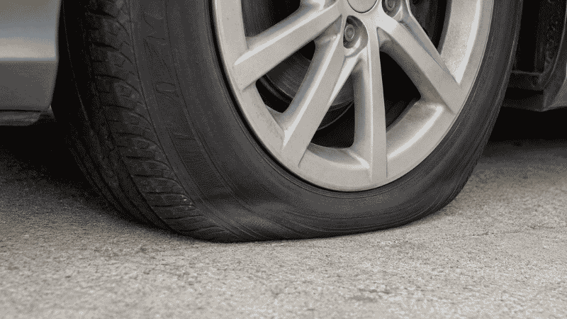 A visibly underinflated car tire with the sidewall bulging at the bottom contact patch, illustrating how low tire pressure changes rolling diameter and can trigger the traction control system