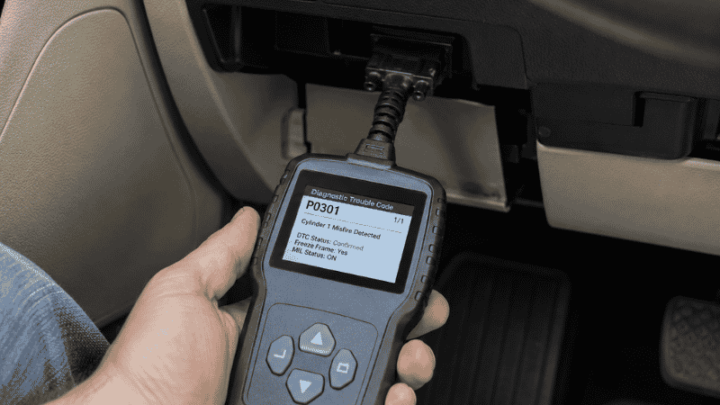 A handheld OBD2 diagnostic scanner plugged into a car's OBD port under the dashboard, displaying ABS or traction control fault codes on its screen