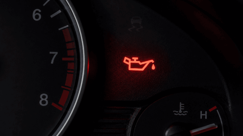 A car dashboard with the red oil pressure warning light illuminated, showing the oil can symbol that indicates critically low oil pressure requiring immediate action