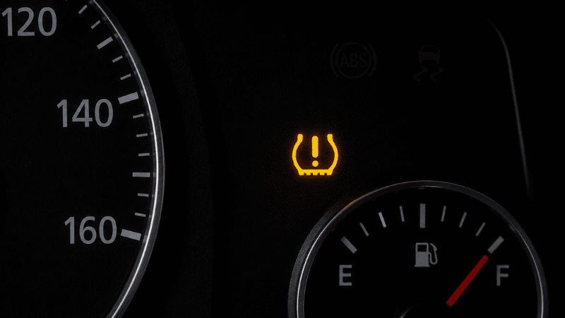 A car dashboard showing the TPMS tire pressure monitoring system warning light illuminated in yellow, showing the horseshoe shape with exclamation mark symbol