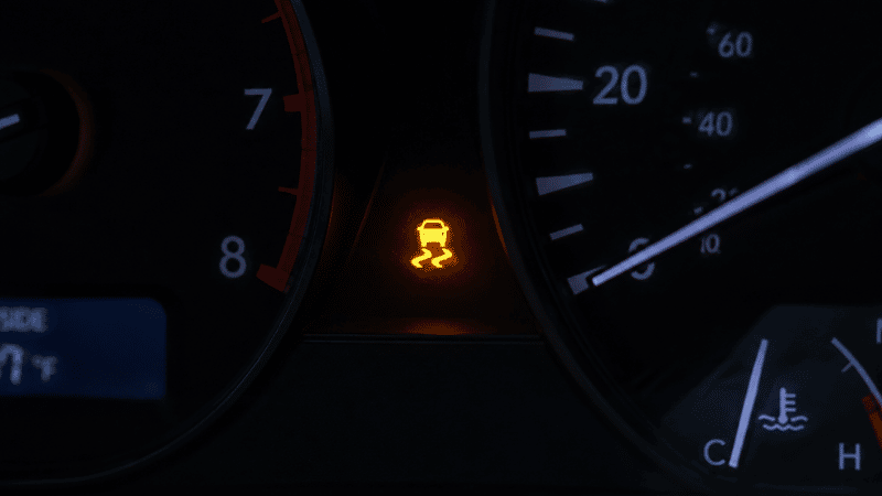 A car dashboard showing the traction control system warning light illuminated in orange, displaying the car-with-squiggly-lines TCS symbol