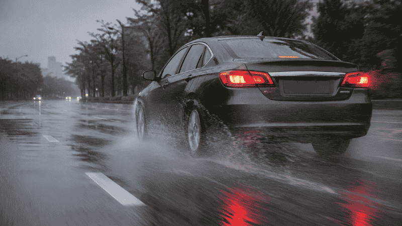 A car accelerating on a wet road with visible tire spray, showing the conditions where the traction control system activates to prevent wheel slip