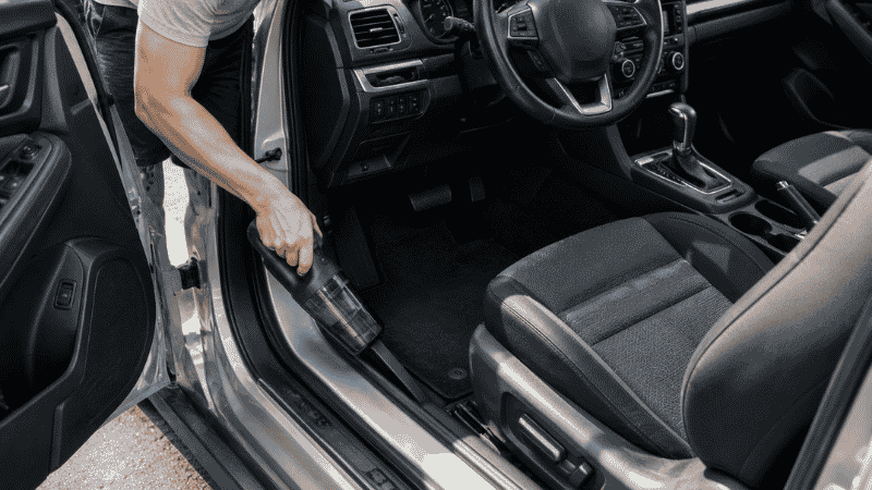 A person quickly vacuuming just the front seat area and floor mat of a car during a 5-minute weekly maintenance routine