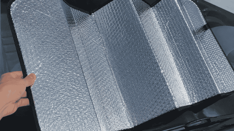 A silver reflective accordion-style car windshield sun shade partially folded showing the accordion fold sections and reflective surface