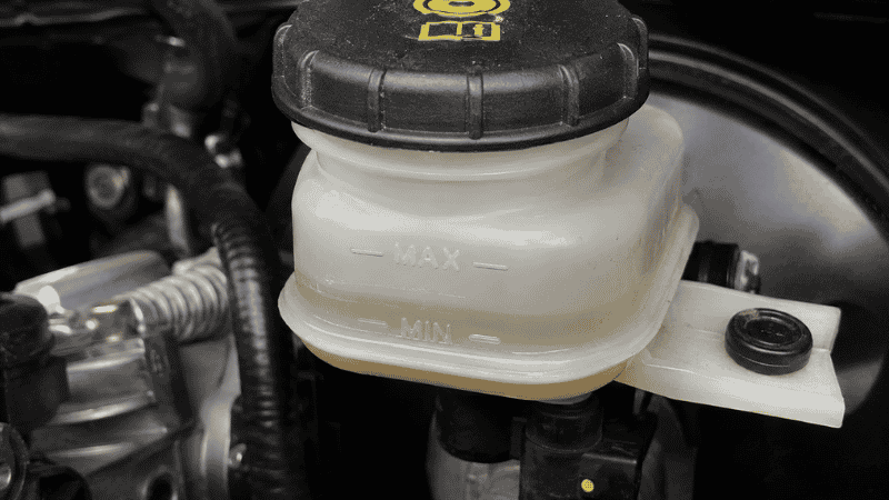 A car brake fluid reservoir showing the fluid level significantly below the minimum mark on the translucent plastic container indicating low brake fluid