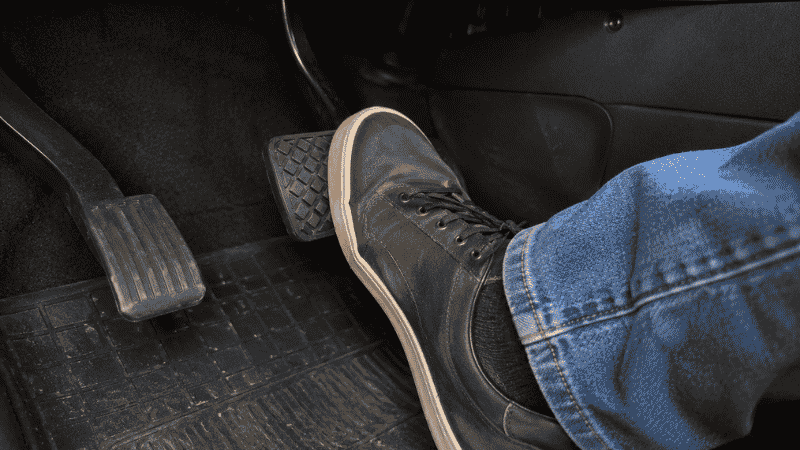 A driver pressing the brake pedal firmly with their foot to test whether it feels firm or spongy as the key diagnostic step when the brake warning light is on