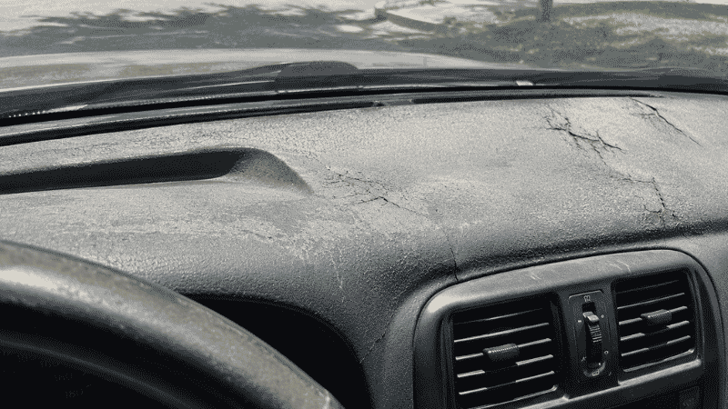 A car interior dashboard showing cracking and damage from prolonged UV exposure and extreme heat, with the sun shining through the windshield