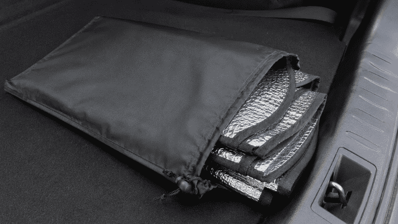 A folded car sun shade stored in a fabric carrying pouch placed in a car trunk or behind the front seat for convenient access