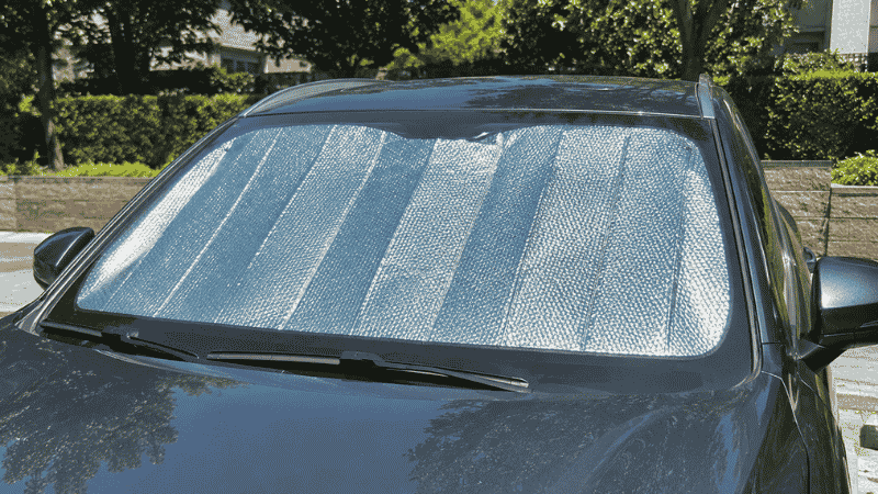 A silver reflective car sun shade installed on a car windshield while parked in a sunny parking lot on a hot summer day