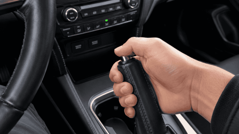 A driver's hand fully releasing the parking brake lever in a car center console, the most common and easily fixed cause of a brake warning light