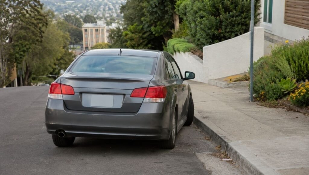 A car parked on a steep residential hill with the front wheels visibly turned toward the curb showing correct downhill parking wheel positioning